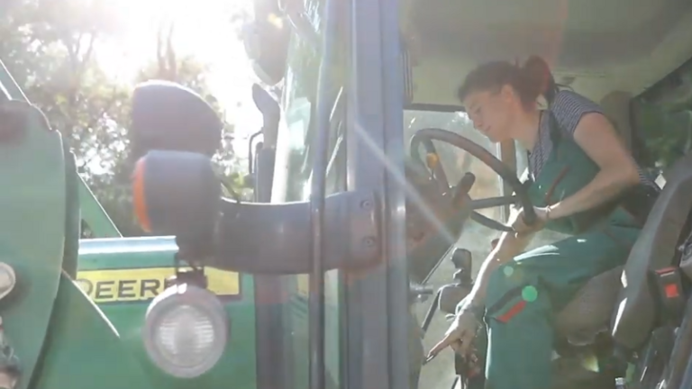Junge Frau in grüner Arbeitshose fährt Traktor